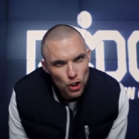 Ed Skrein has a bald look and is rapping directly looking at the camera.